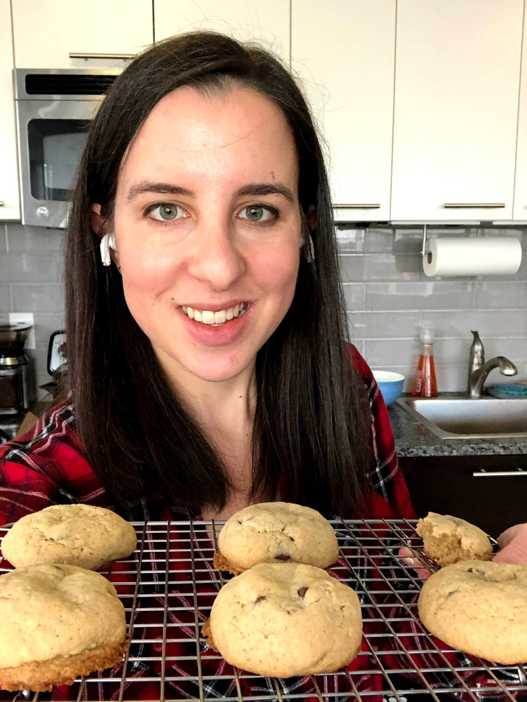 Image showing a woman with dark brown hair looking into the camera while holding up a tray of puffy-looking cookies, which are actually bread-like cookies.