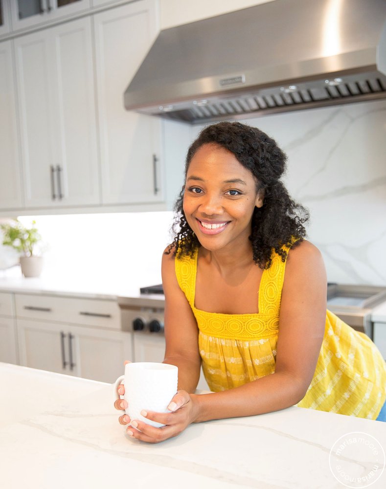 Marissa Moore leans on a counter smiling and holding a coffee mug.